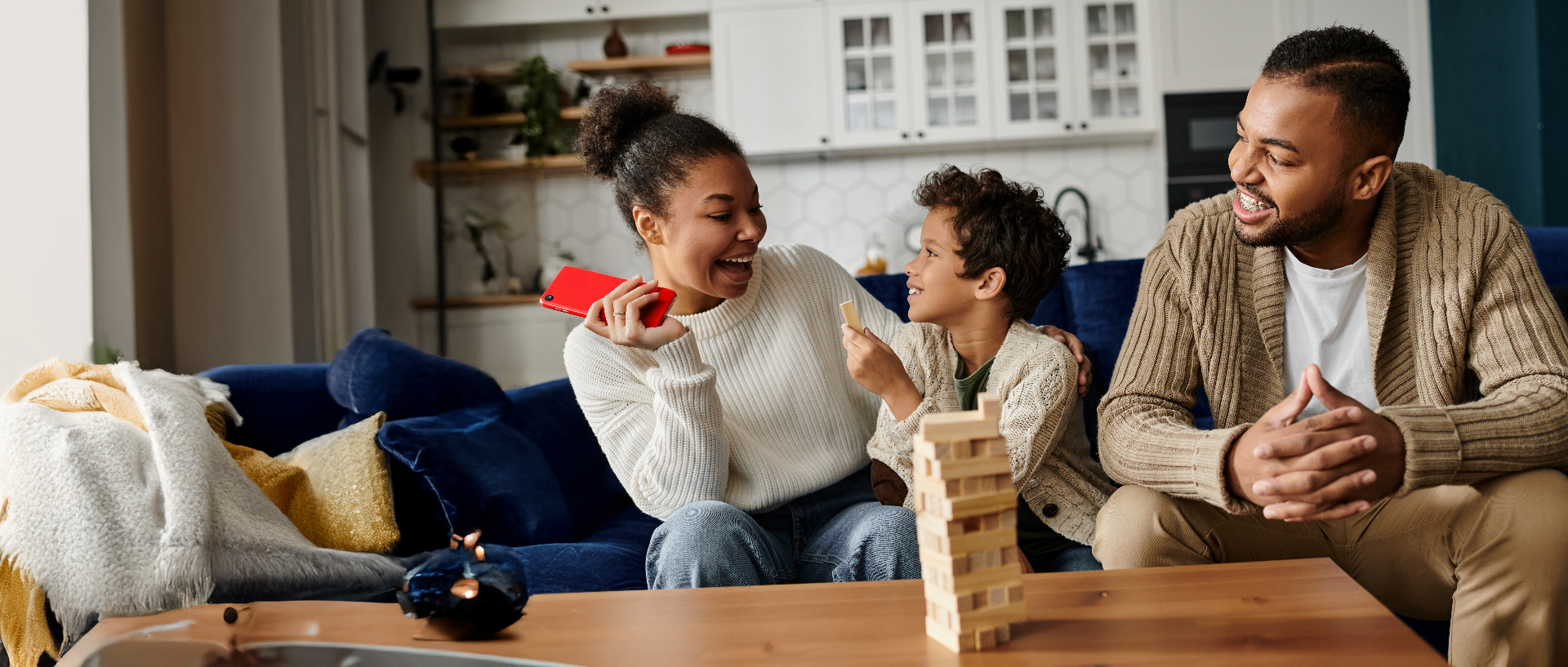 A family on a couch playing a wooden block game together, laughing in warm evening light